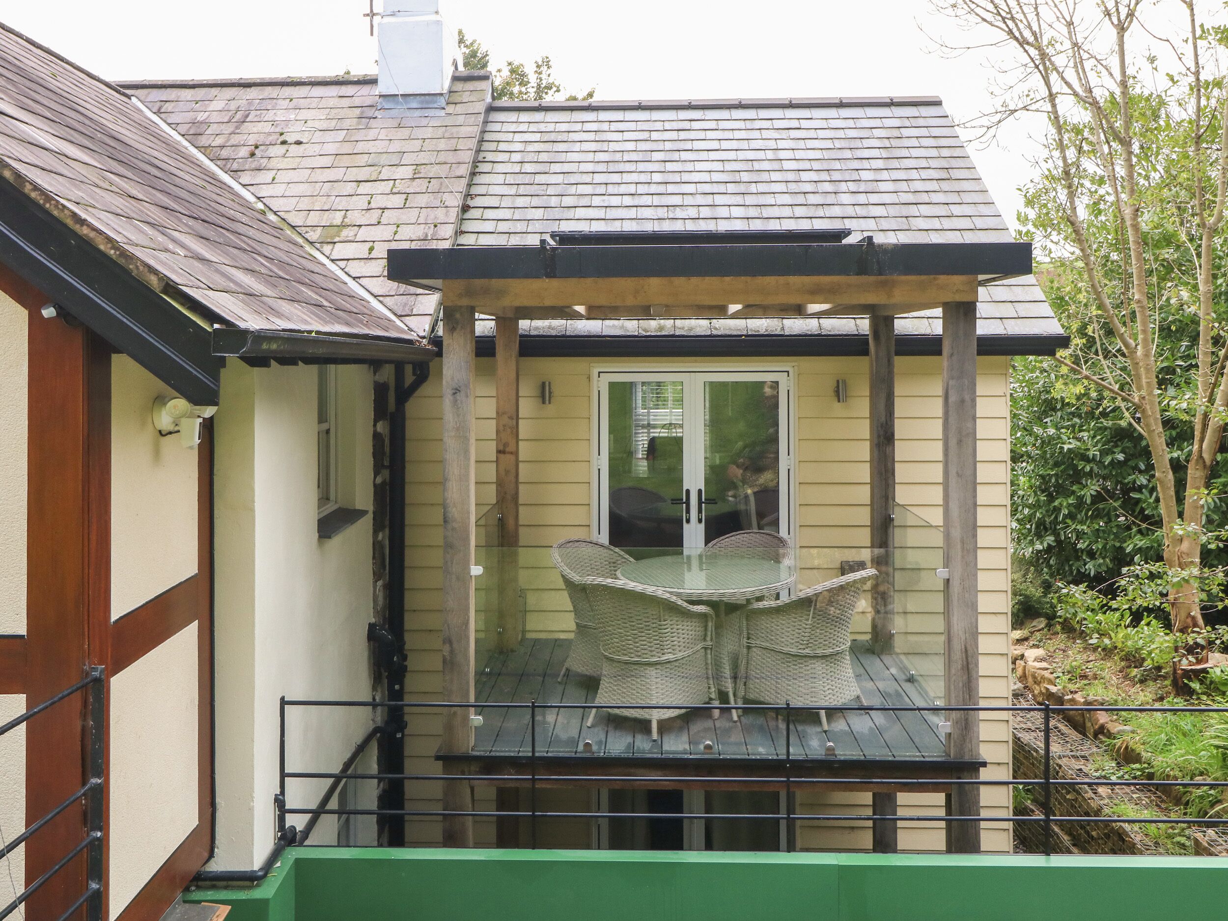 A covered outdoor seating area with a glass enclosure, a table, and chairs.