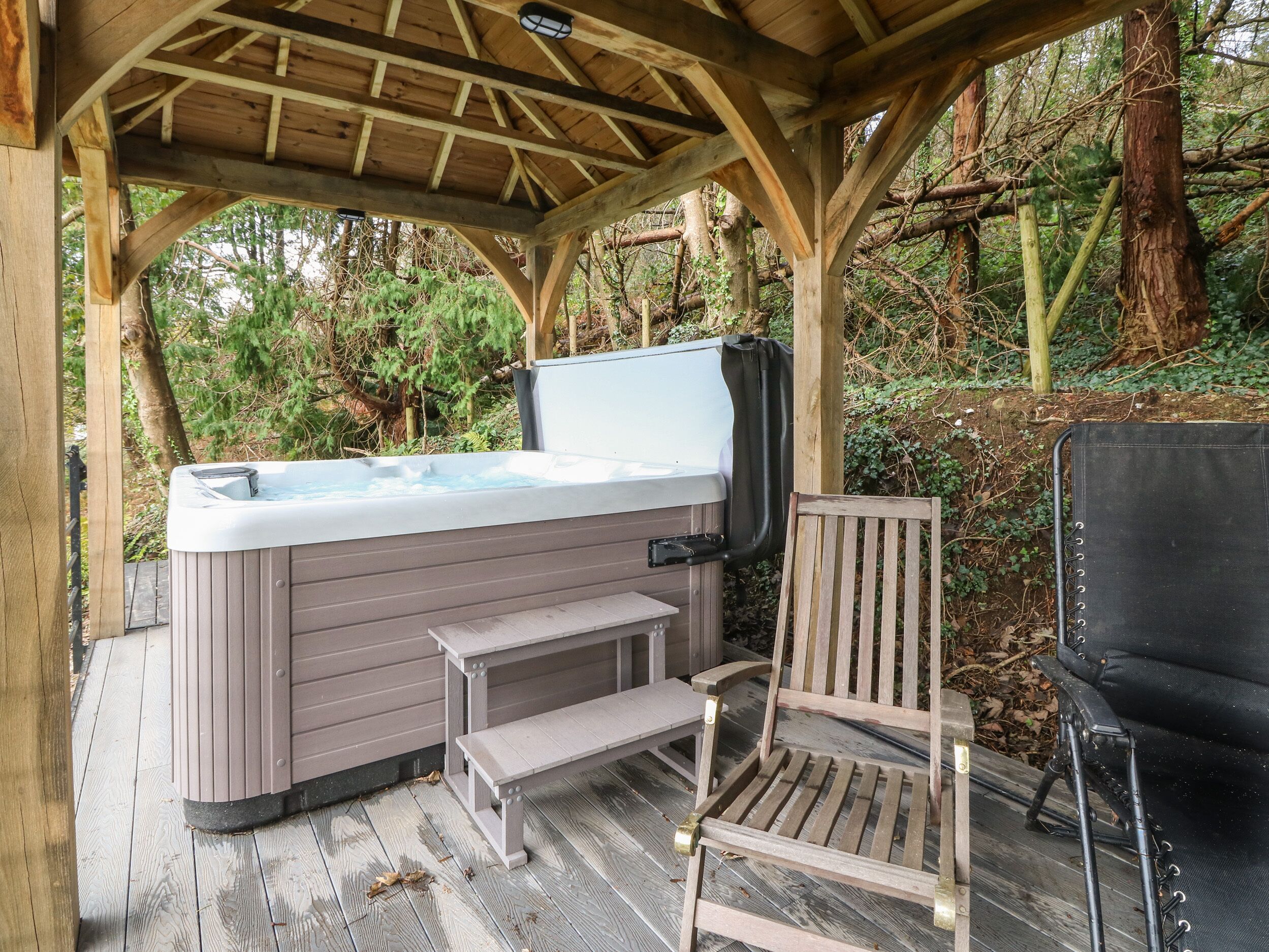 Una terraza de madera con un jacuzzi, un banco y una silla.