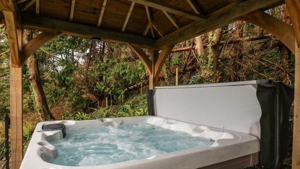 A hot tub under a wooden pergola surrounded by trees.