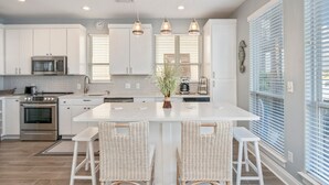 A modern kitchen with white cabinetry, stainless steel appliances, and a central island with bar stools.