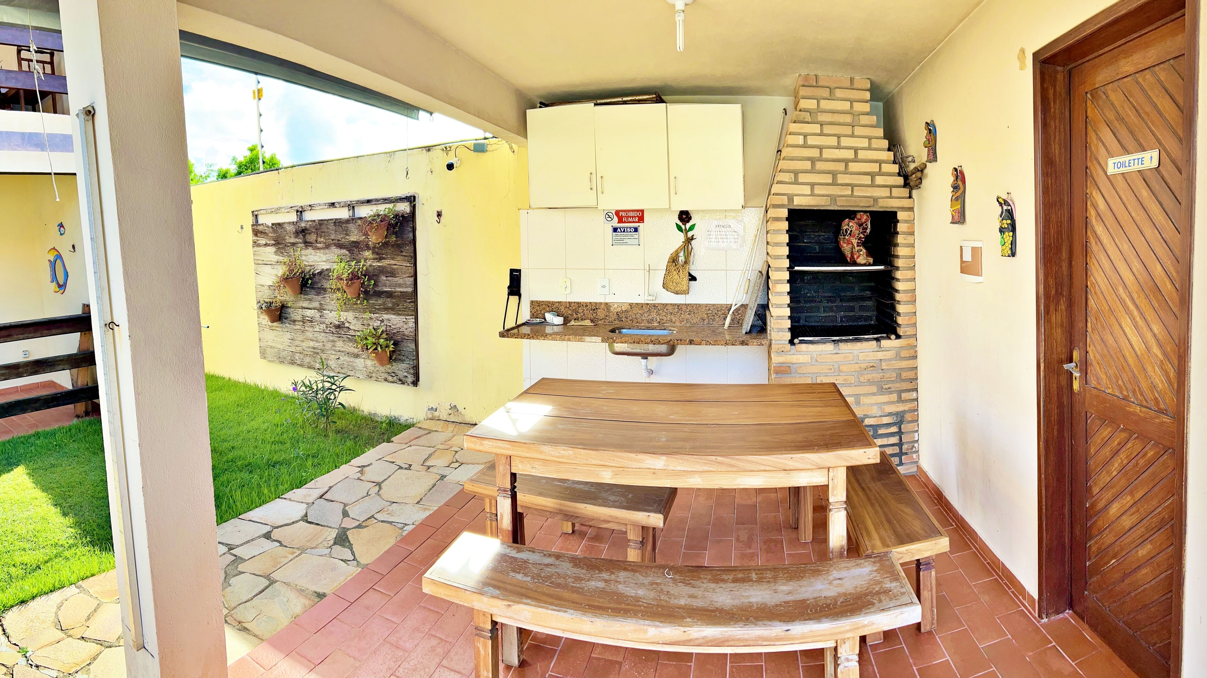 A patio area with a wooden table and benches, a brick oven, a sink, and a cabinet with a sign.