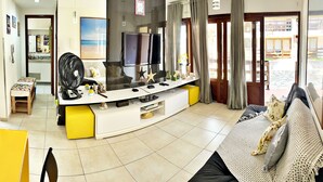 Una sala de estar con un televisor de pantalla plana grande, un sofá, una mesa de centro y una mesita con un ventilador.
