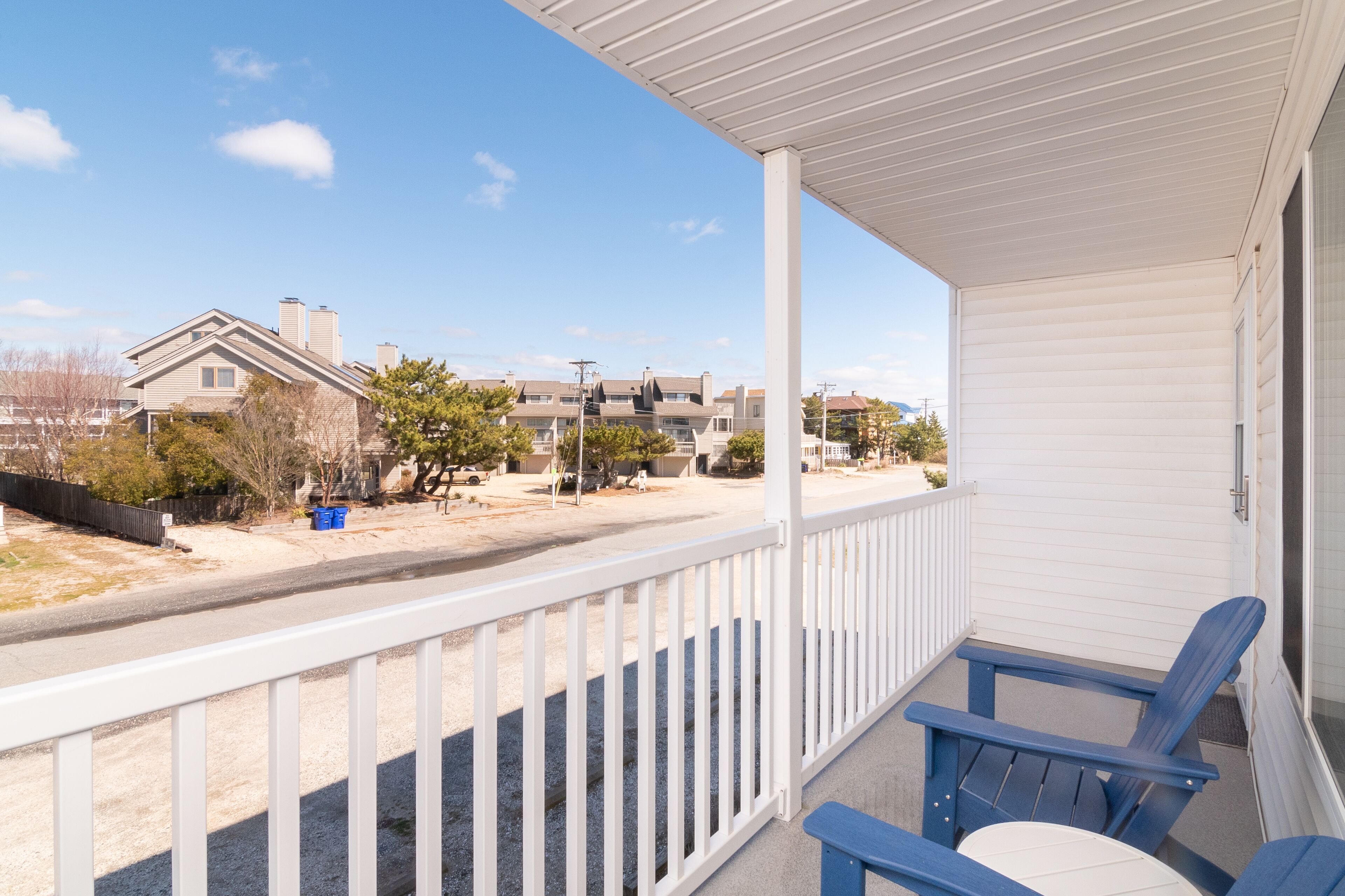 A covered balcony with white railings and blue chairs.