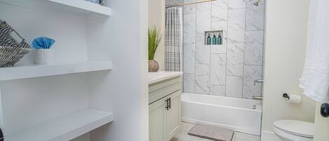 Une salle de bain équipée d’une baignoire, de toilettes, d’étagères contenant des articles de toilette et d’un rideau de douche.