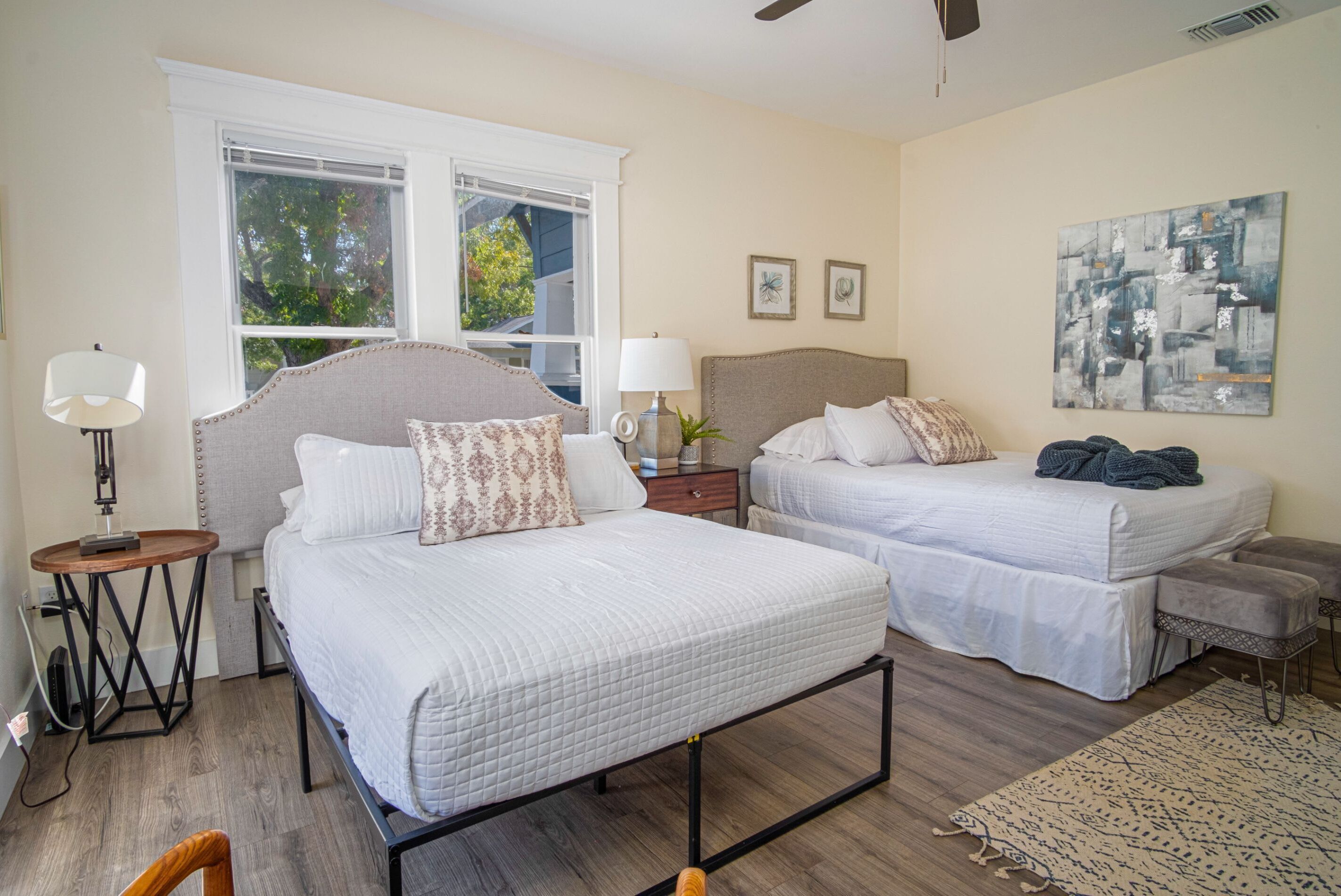 A bedroom with two beds, a window, a lamp, and a painting.