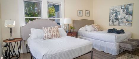A bedroom with two beds, a window, a lamp, and a painting.