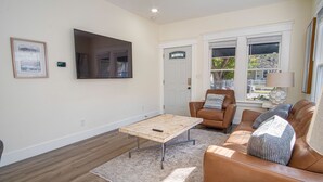Een woonkamer met een bruine leren bank, een houten salontafel en een grote flatscreen televisie aan de muur.