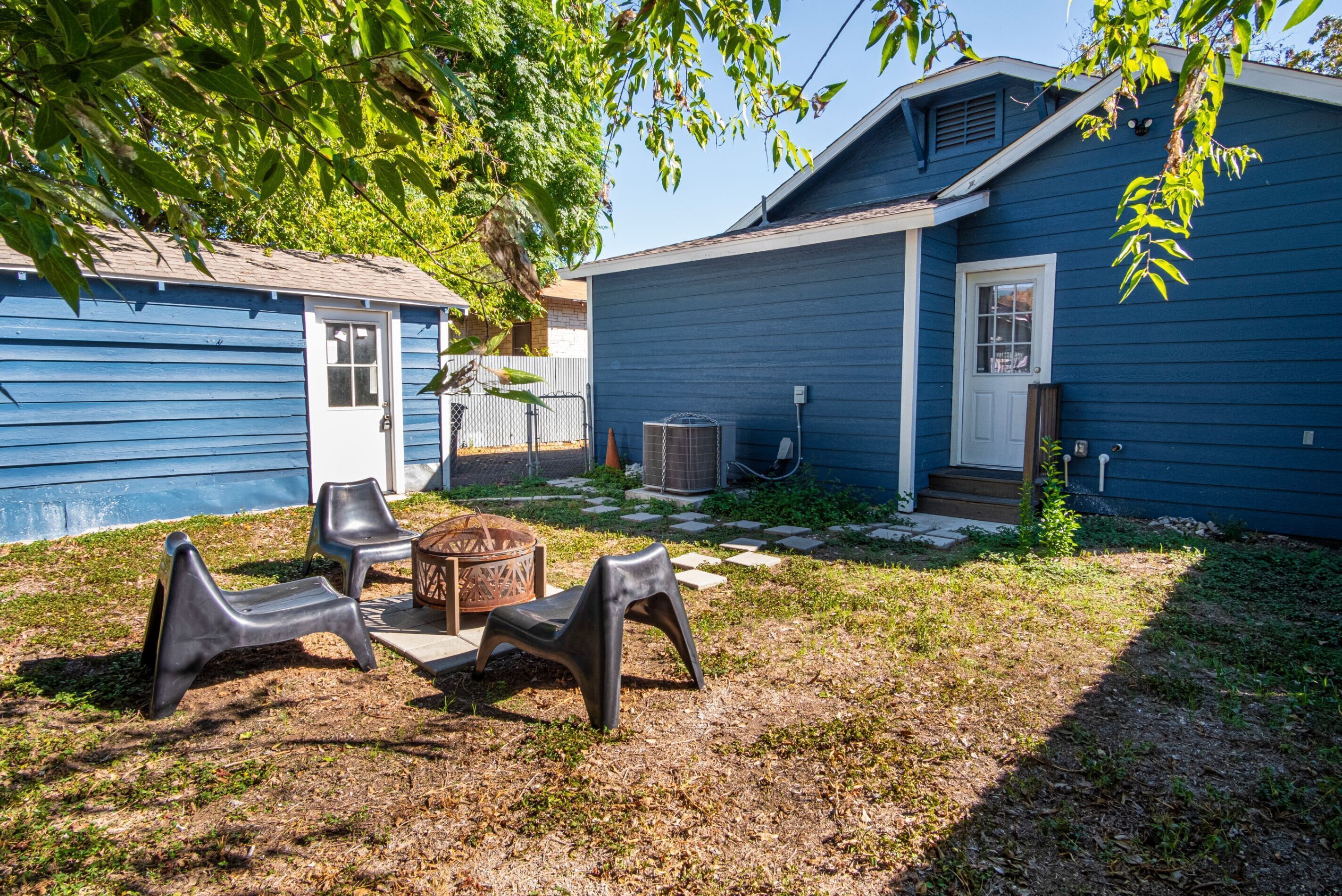 A backyard with a blue house, outdoor furniture, a fire pit, and a covered patio area.