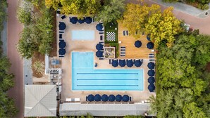 An aerial view of a hotel with a large rectangular pool, multiple lounge areas with umbrellas, and a checkered area near the pool.