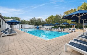 Ein Swimmingpool mit Liegestühlen und Sonnenschirmen, umgeben von einer gefliesten Terrasse.