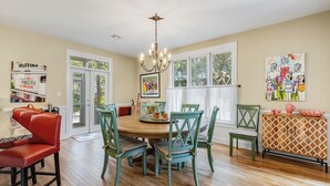 A dining room with a wooden table and chairs, a chandelier, and a view of the outdoors through large windows.