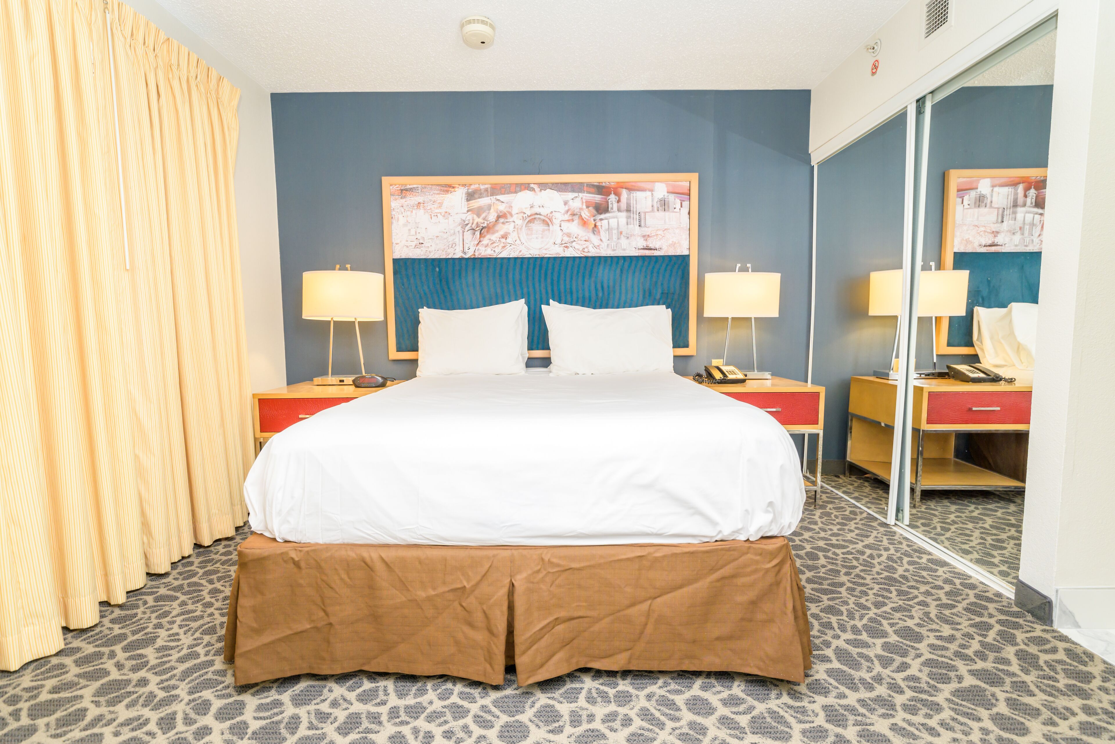 A hotel room with a large bed, two bedside tables with lamps, a mirror, and a patterned carpet.