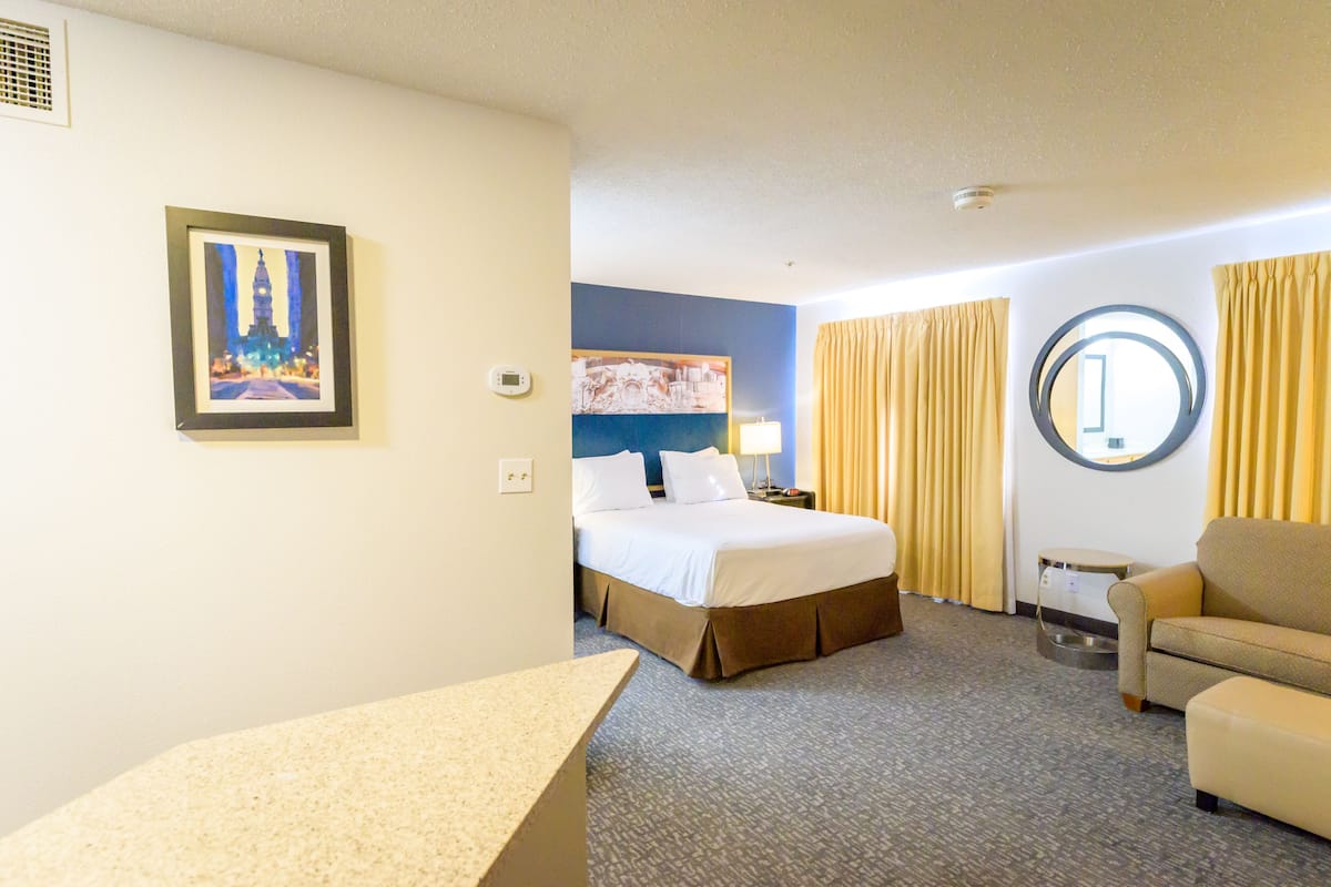 A hotel room with a bed, a desk, a chair, a round mirror, and a painting on the wall.