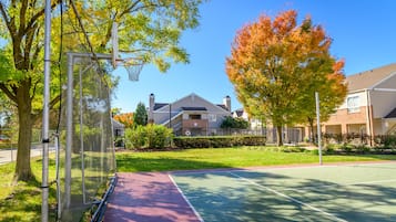 Un terrain de basket en plein air, équipé d’un panier, entouré d’arbres et de bâtiments résidentiels.