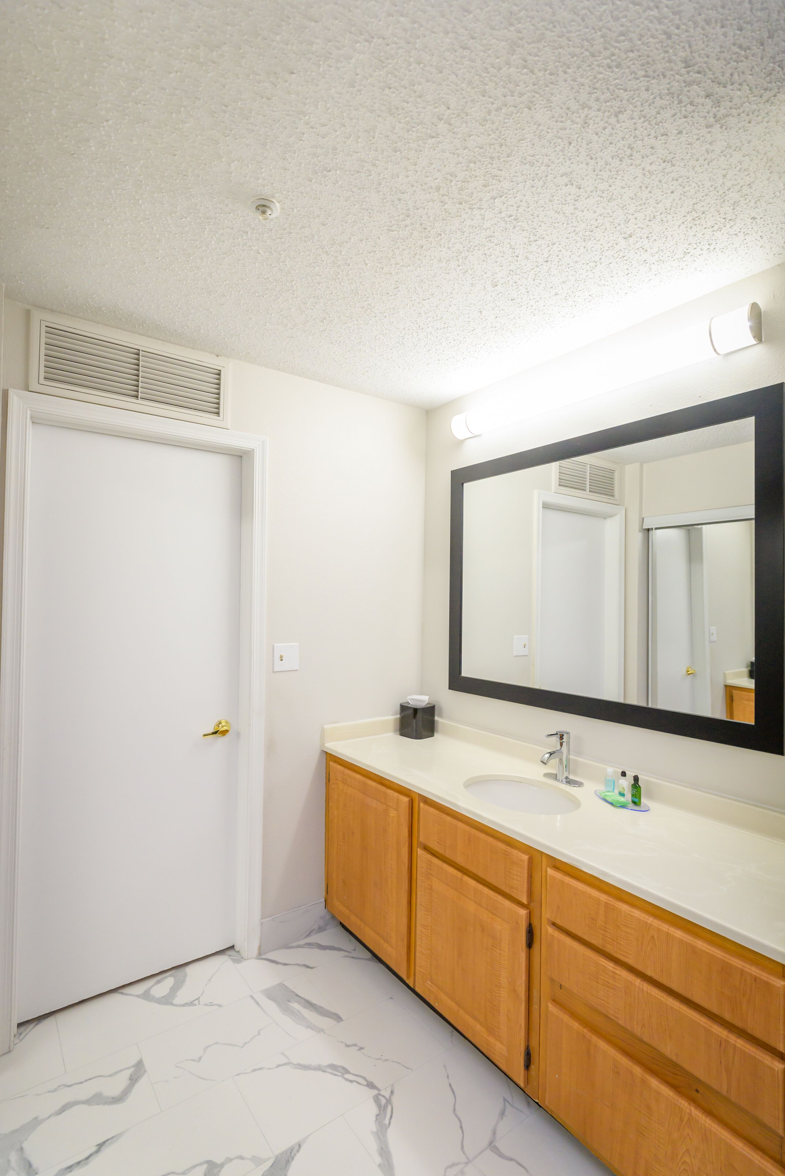 A bathroom with a white door, a large mirror, a sink, and wooden cabinets.