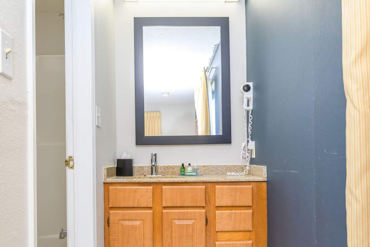A bathroom with wooden cabinets, a marble floor, a mirror, and a hairdryer on the wall.
