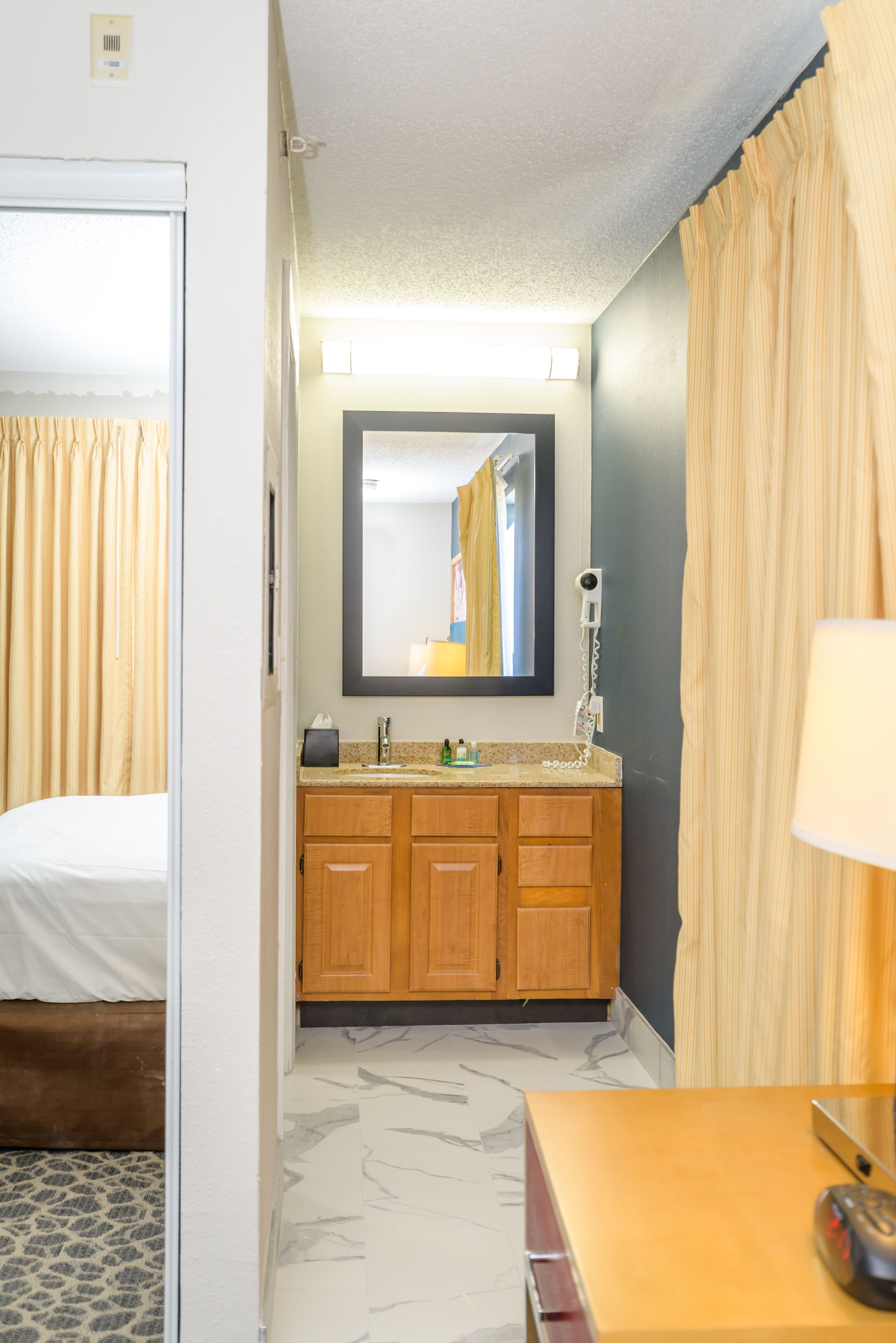 Una habitación de hotel con una cama, armarios de madera, un espejo y una lámpara.