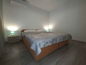 A bedroom with a bed, bedside lamps, a nightstand, and a wall-mounted air conditioner.