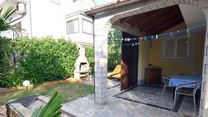 A patio area with a stone floor, a table with chairs, and a grill.
