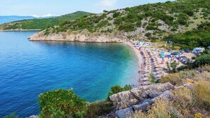 A coastal beach with clear blue waters, rocky cliffs, and lush greenery.