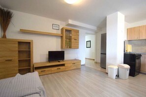 A modern apartment with a TV, wooden furniture, a kitchen, and a dining area.