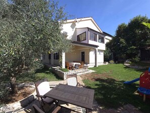 A two-story house with a patio, a table and chairs, and a small garden.