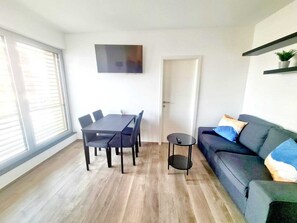 Ein modernes Wohnzimmer mit Esstisch, Stühlen, einer Couch, einem an der Wand befestigten Fernseher und einer Tür.