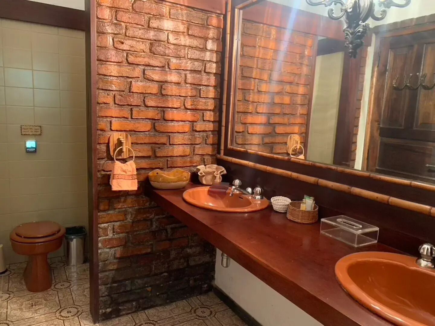 A bathroom with a brick wall, two sinks, a mirror, and a toilet.