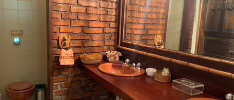 A bathroom with a brick wall, two sinks, a mirror, and a toilet.
