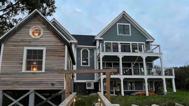 A two-story house with a wooden deck leading to a stone pathway. - The Sea Eagle - Luxury 5 BR Waterfront Home in Boothbay Harbor with Dock & Sauna (Boothbay Harbor)