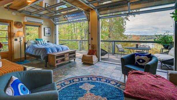 A spacious room with a bed, a sofa, a chair, and a balcony with a view of trees.