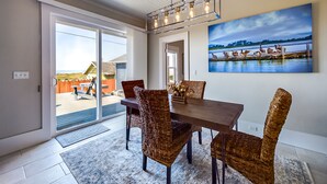 A dining area with a wooden table and wicker chairs, a ceiling light fixture, and a painting of birds on a water body. - Sunset Bliss, Oceanview, Luxury, Hot Tub (Samoa)