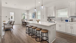 A modern kitchen with a large island, bar stools, and a dining area with a sofa and chairs. - 4BR w/2 Master Suites, Golf Cart, .3 Mi to Beach, Sleeps 15 + Free Tickets! (Santa Rosa Beach)