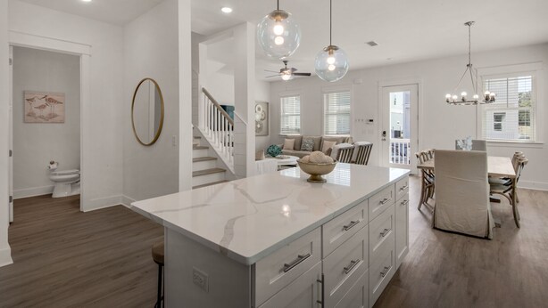 A modern kitchen with a marble island, pendant lights, and a dining area with a wooden table and chairs. - 4BR w/2 Master Suites, Golf Cart, .3 Mi to Beach, Sleeps 15 + Free Tickets! (Santa Rosa Beach)