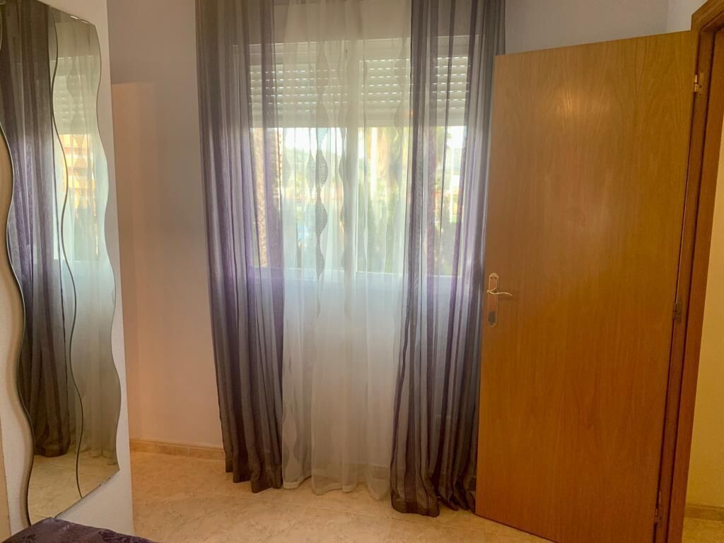 A room with a wooden door, sheer curtains, and a mirror on the wall.