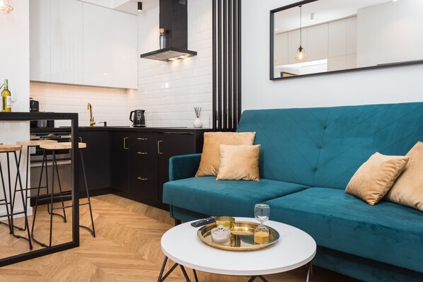Una cocina moderna con armarios blancos, encimera negra y sofá verde azulado con cojines color beige.