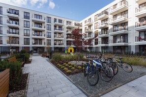 Un moderno edificio de apartamentos con varios balcones, un patio central con un parque infantil y bicicletas estacionadas afuera.