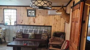 A rustic interior with a wooden floor, a sofa set, a dining table, and a deer head mounted on the wall. - 3 bed/2 bath riverside cabin (Byrnedale)