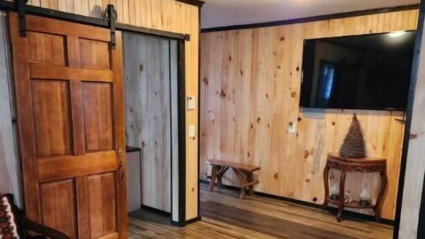 A room with wooden walls and floors, a sliding door, a bench, a small table, and a television. - 3 bed/2 bath riverside cabin (Byrnedale)