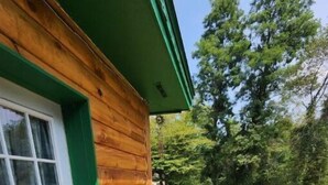 A wooden cabin with a green door and window, a wooden deck, and a wooden fence. - 3 bed/2 bath riverside cabin (Byrnedale)