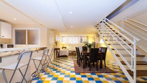 Une chambre d’hôtel avec un sol à carreaux, un coin repas avec des chaises et une table, un coin cuisine avec un comptoir et des appareils électroménagers, et un escalier avec une rampe.