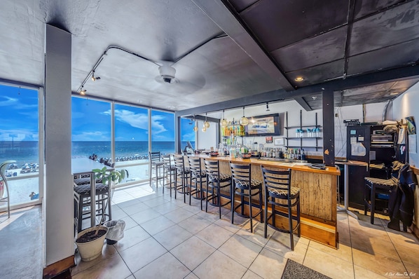 Un espace bar avec vue sur la plage, des tabourets de bar et un comptoir où sont exposées différentes bouteilles.