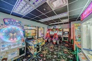 Une salle d’arcade proposant divers jeux, un présentoir pour les prix et un sol décoré de motifs en forme d’étoiles.