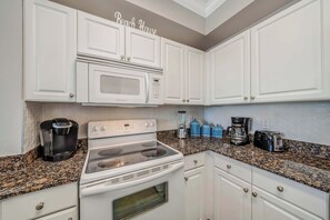 A kitchen with white cabinets, a microwave, a stove, a coffee maker, and a toaster. - Tidewater1418 Corner Views WOW, FREE Golf&Perks, Pools, Hot Tubs by Pier Park (Panama City Beach)