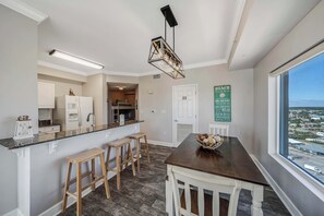 Una cocina moderna con una mesa de madera oscura, taburetes de bar y vista a la playa a través de un ventanal grande.