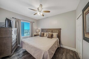 A bedroom with a bed, a ceiling fan, a dresser, a window with curtains, and a door. - Tidewater1418 Corner Views WOW, FREE Golf&Perks, Pools, Hot Tubs by Pier Park (Panama City Beach)