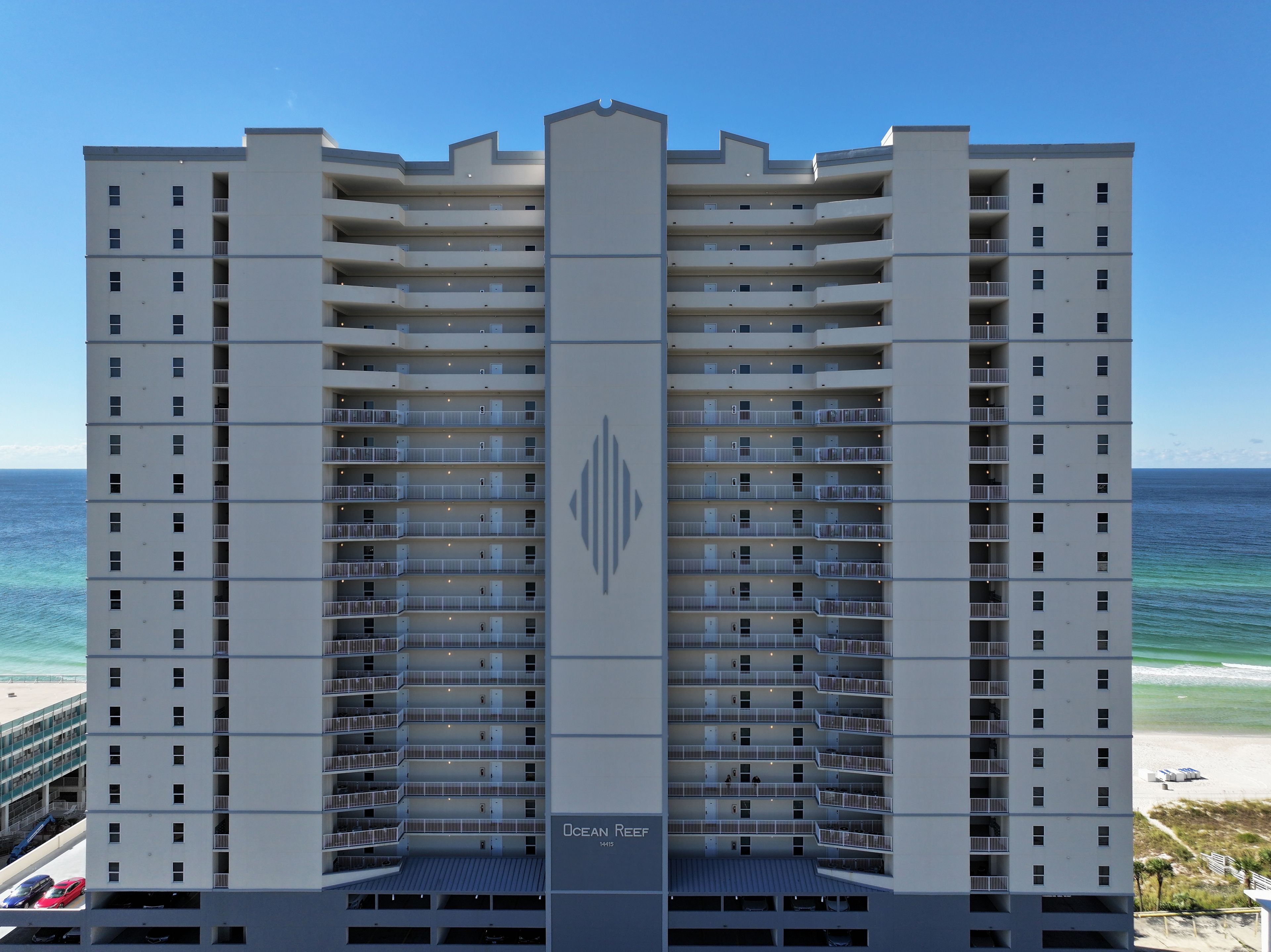 A multi-story hotel with balconies, a central entrance, and a view of the ocean.