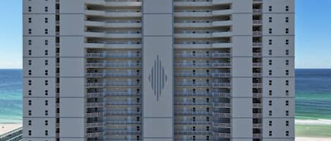 Un hotel de varios pisos con balcones, una entrada central y vista al océano.