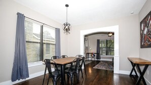 A dining area with a wooden table and black chairs, a hanging light fixture, and a view through a window with blinds. - 2BR Luxury EADO House! Medical Center, Stadiums ⭐️⭐️⭐️⭐️⭐️ (Houston)