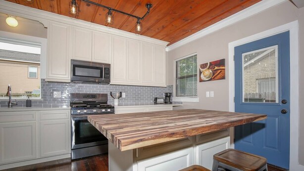 A kitchen with white cabinets, a wooden countertop, a blue door, and a hanging light fixture. - 2BR Luxury EADO House! Medical Center, Stadiums ⭐️⭐️⭐️⭐️⭐️ (Houston)
